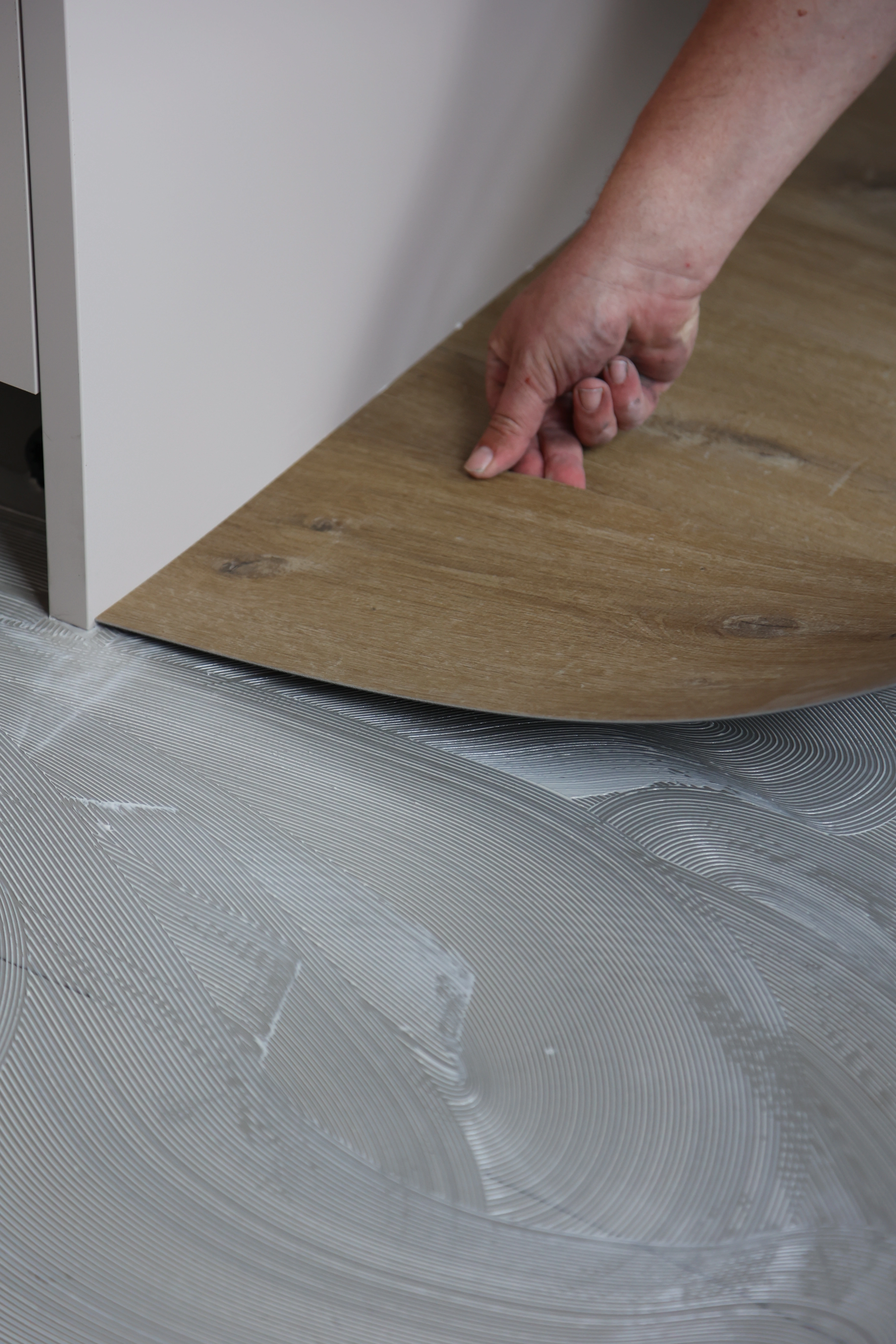 Hand van vakman plaatst pvc vloer op verse lijmlaag